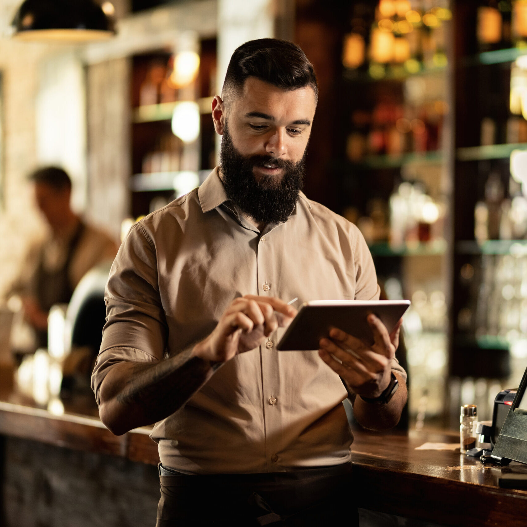 Young smiling waiter using touchpad while working in a pub.